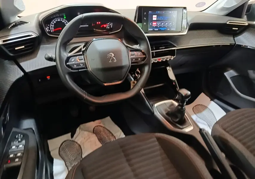 Vue intérieure avant de la Peugeot 208 gris clair, volant cuir multifonctions et écran tactile central visible.