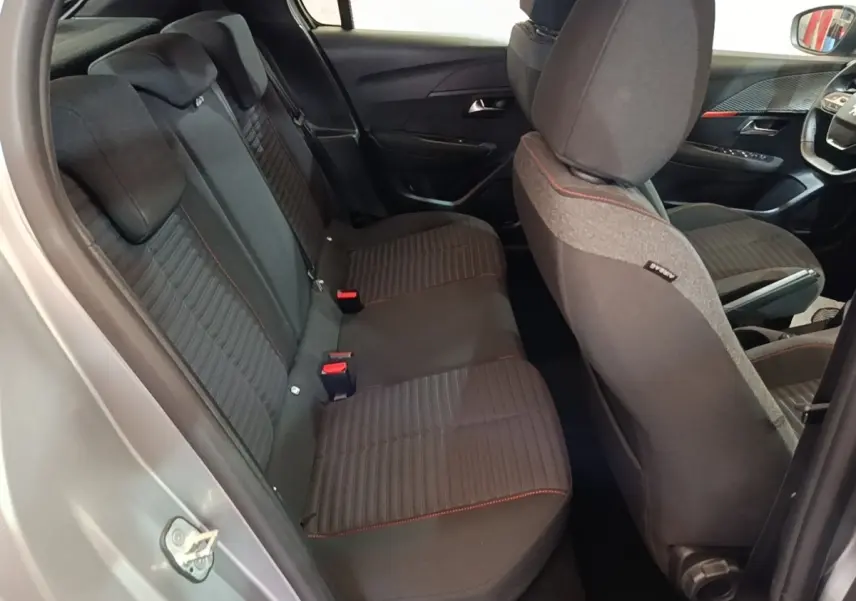 Vue intérieure côté arrière droit de la Peugeot 208 gris clair, montrant la banquette arrière noire avec surpiqûres rouges.
