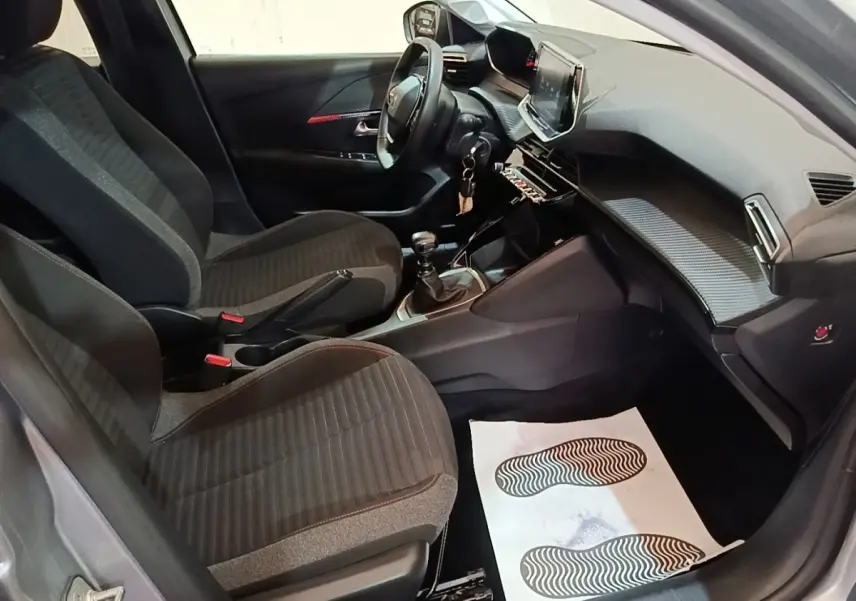 Vue intérieure côté conducteur de la Peugeot 208 gris clair 2023, volant cuir multifonctions et tableau de bord moderne.