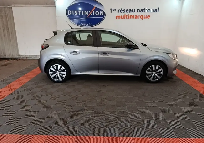 Profil droit d'une Peugeot 208 gris clair 2023 garée en intérieur sur sol à damier noir et rouge.