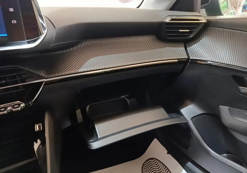 Vue intérieure côté passager du tableau de bord gris foncé avec boîte à gants ouverte et finition effet carbone sur Peugeot 208 2023.