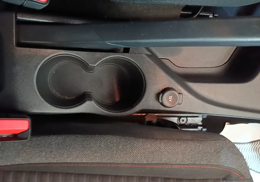 Gros plan sur la console centrale noire avec porte-gobelets et prise 12V dans une Peugeot 208 gris clair.