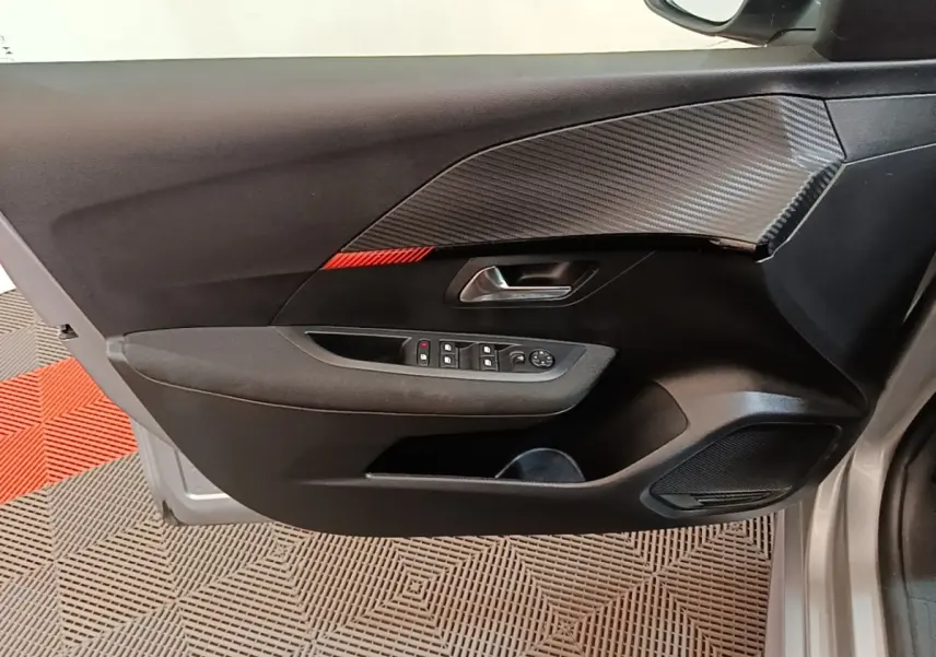 Vue intérieure côté gauche de la porte avant gris clair d'une Peugeot 208 avec insert effet carbone et commandes électriques.