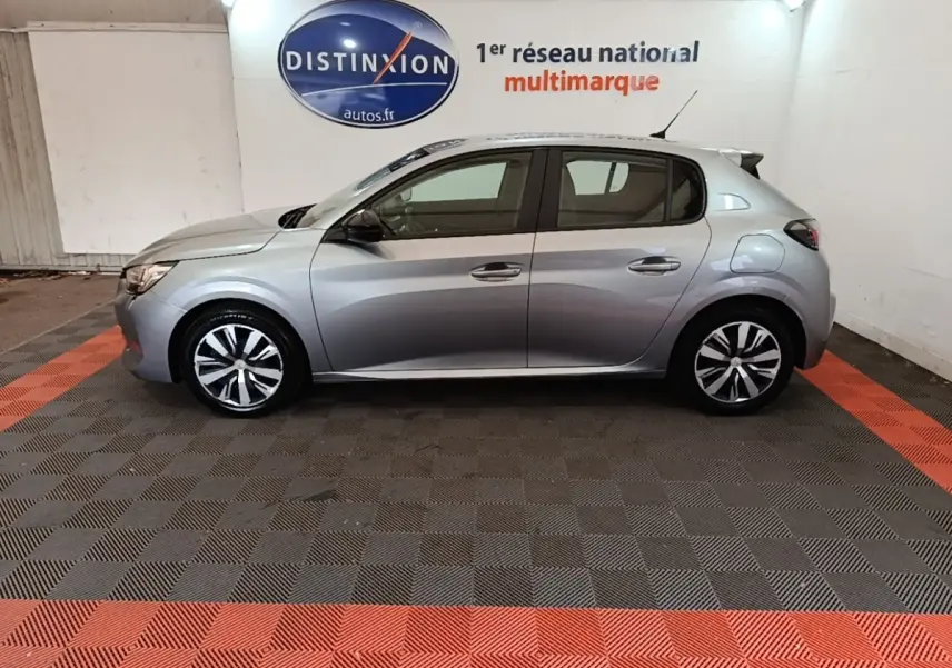 Profil droit d'une Peugeot 208 gris clair 2023 garée en intérieur sur sol à damiers noir et rouge.