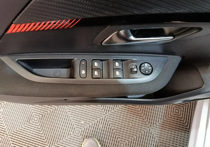 Vue rapprochée de la porte côté conducteur d'une Peugeot 208 2023, montrant les commandes des vitres et rétroviseurs.