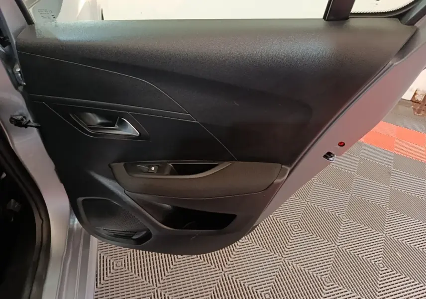 Vue rapprochée de la porte arrière gauche gris clair d’une Peugeot 208 2023 avec panneau intérieur noir et commande de vitre.