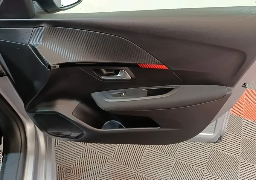 Vue intérieure de la porte avant gauche du Peugeot 208 gris clair, avec insert carbone et bande rouge décorative.