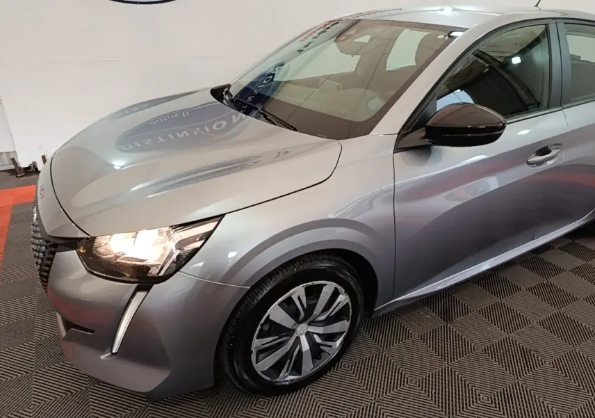 Peugeot 208 gris clair vue 3/4 avant droit avec phares allumés et jantes alliage distinctives.