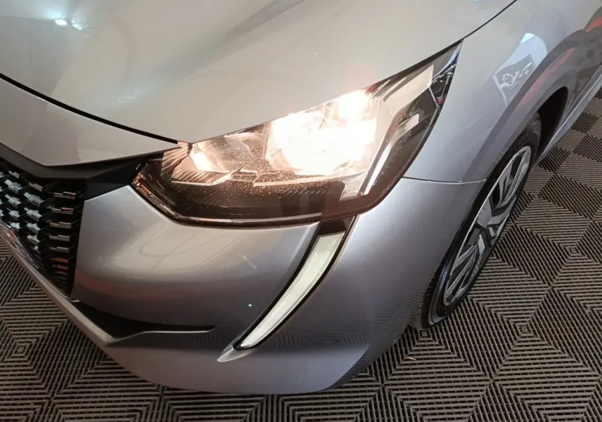 Gros plan sur l'avant droit gris clair de la Peugeot 208 2023 avec phare allumé et jante visible.