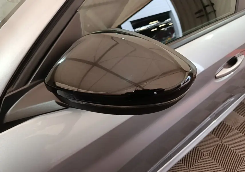 Gros plan sur le rétroviseur noir brillant côté conducteur d’une Peugeot 208 gris clair, vue de profil.