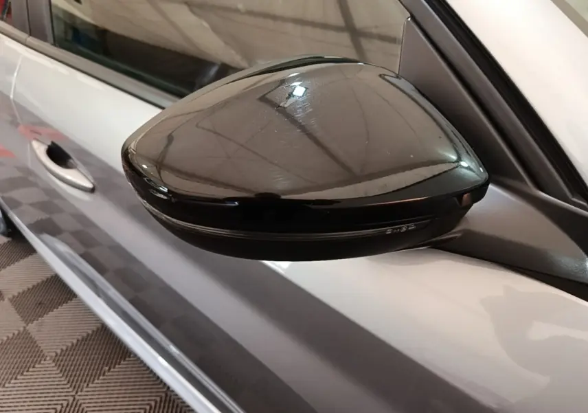 Rétroviseur noir brillant côté gauche d'une Peugeot 208 gris clair vue en gros plan depuis l'avant.