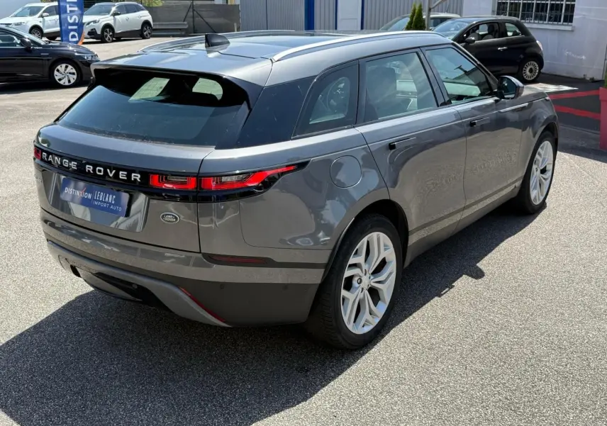 Vue 3/4 arrière droite d'un Range Rover Velar gris métallisé avec jantes blanches et feux arrière LED distinctifs.