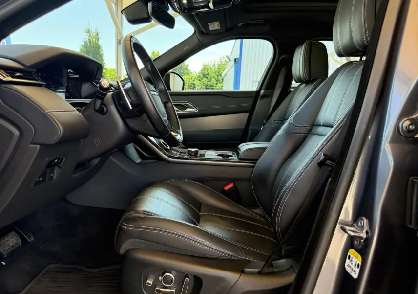 Intérieur côté conducteur du Range Rover Velar gris 2019, sièges en cuir noir avec surpiqûres blanches et tableau de bord moderne.