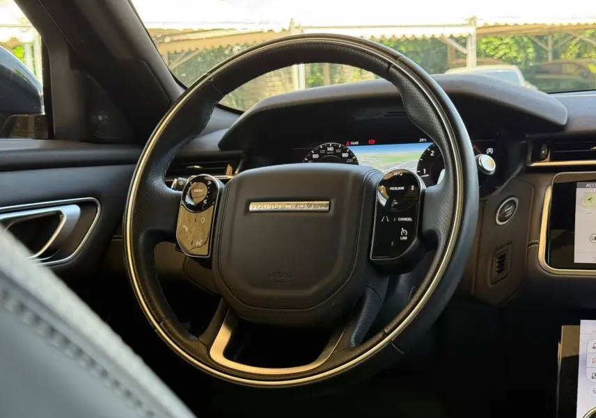 Vue intérieure centrée sur le volant cuir noir du Range Rover Velar 2019 avec tableau de bord numérique et écran tactile.