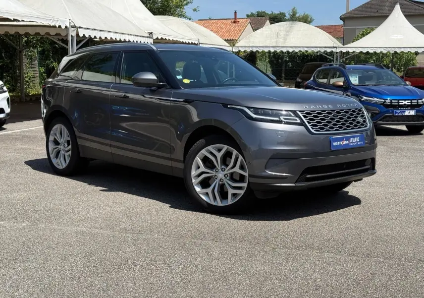 Range Rover Velar gris en 3/4 avant droit, avec jantes alliage et calandre distinctive sur parking extérieur.