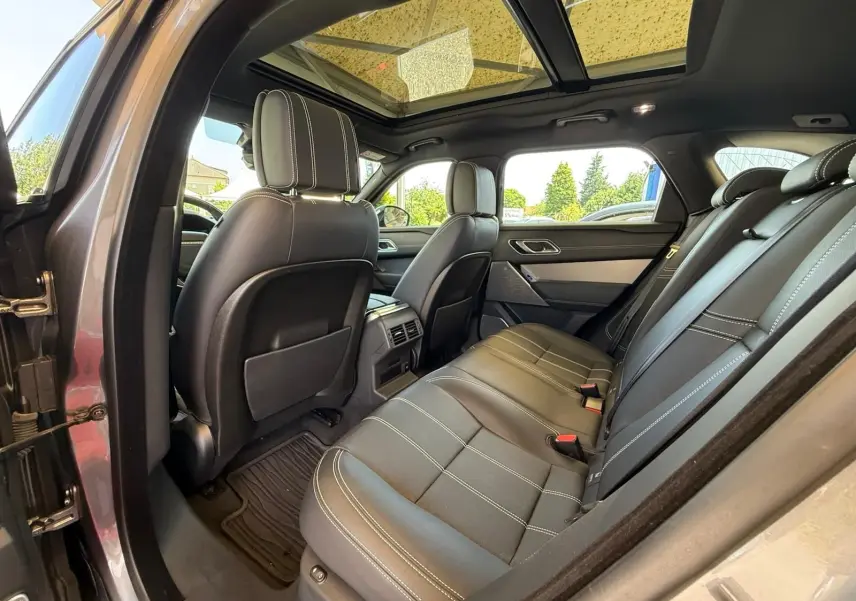 Intérieur arrière du Range Rover Velar gris 2019, vue côté gauche avec sièges cuir noirs et toit panoramique.