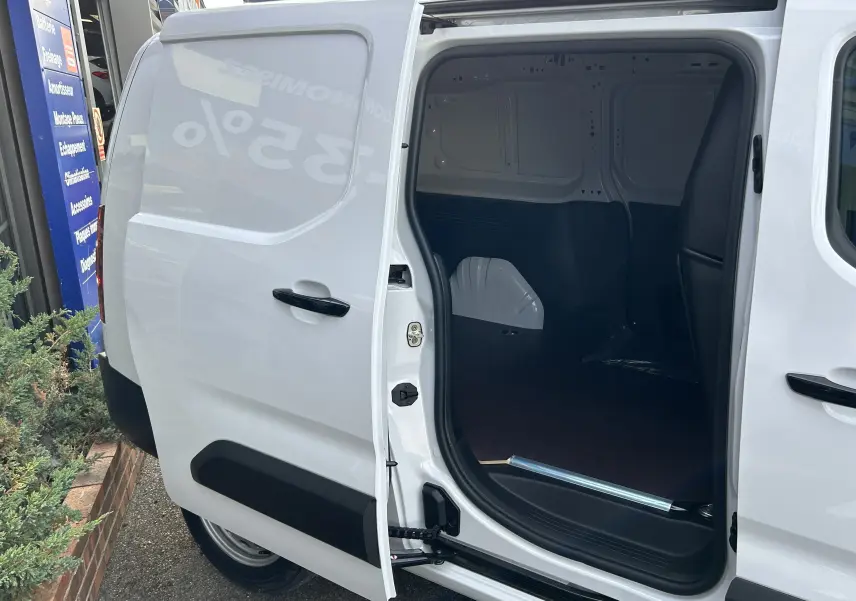 Vue latérale gauche du Peugeot Partner Fourgon blanc 2025 avec porte coulissante ouverte dévoilant plancher bois intérieur.