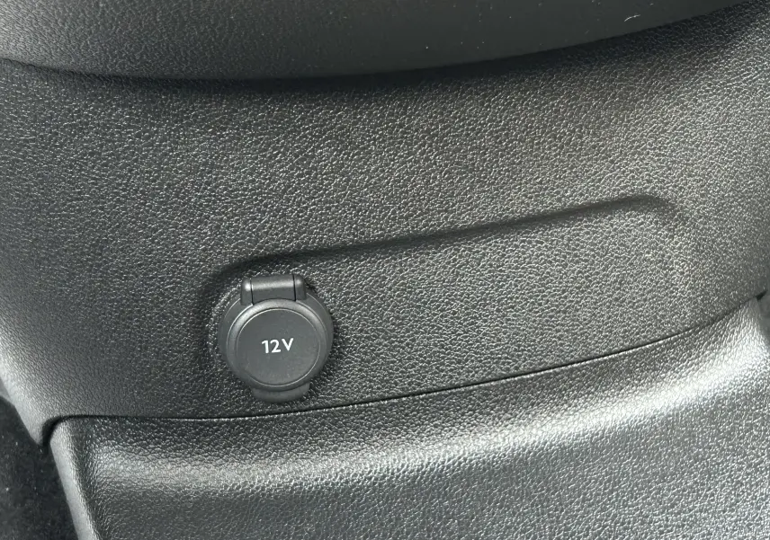 Prise 12V intégrée dans la console centrale noire du Peugeot Partner Fourgon blanc, vue intérieure rapprochée.