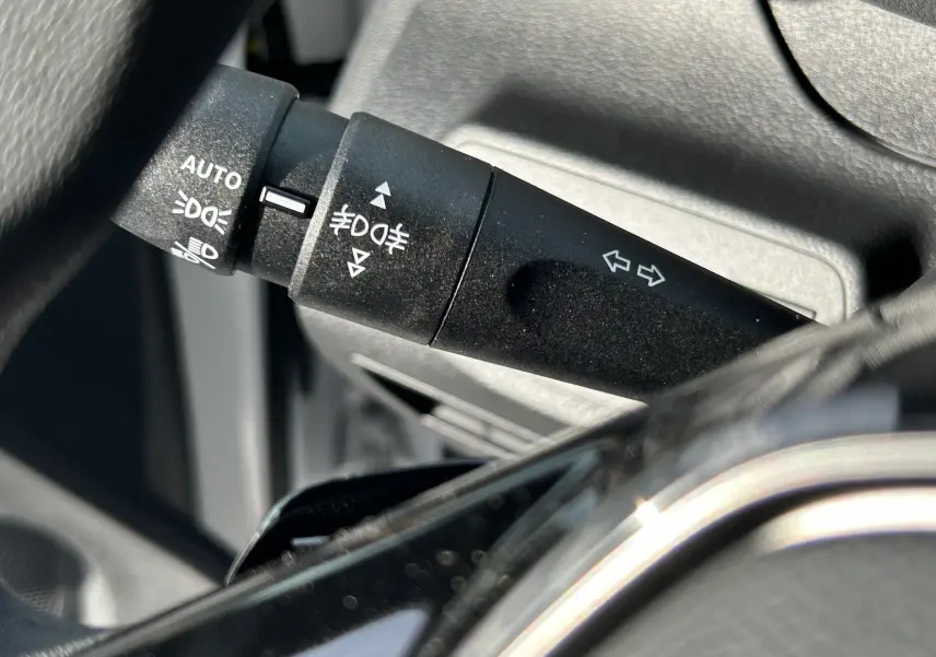 Gros plan sur la manette de clignotants noire à gauche du volant dans l'habitacle d'un Peugeot Partner Fourgon blanc.