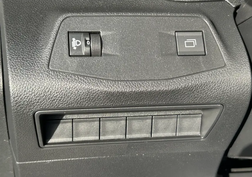 Gros plan sur les commandes de réglage des phares et bouton multifonction dans l'habitacle noir du Peugeot Partner Fourgon blanc.