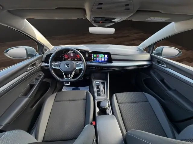 Vue intérieure avant de la Volkswagen Golf VIII gris lunaire, avec tableau de bord numérique et écran tactile central.