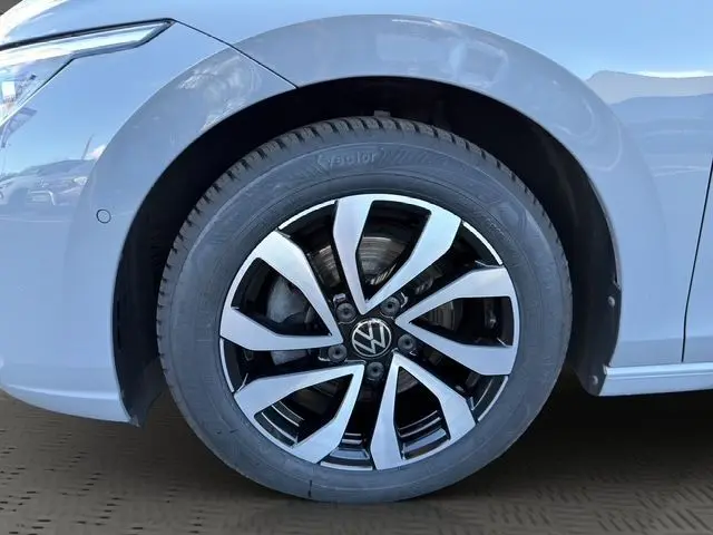 Gros plan sur la roue avant droite d'une Volkswagen Golf VIII gris lunaire avec jante alu bicolore au design moderne.