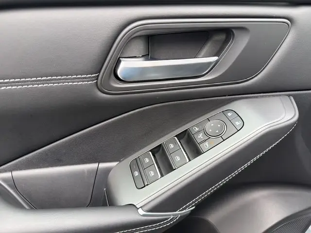 Détail de la porte côté conducteur du Nissan Qashqai gris foncé 2025, avec commandes électriques des vitres et poignée argentée.