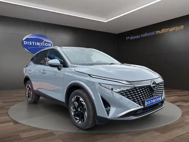 Vue 3/4 avant d'un Nissan Qashqai gris foncé avec calandre noire texturée et jantes noires en exposition showroom.