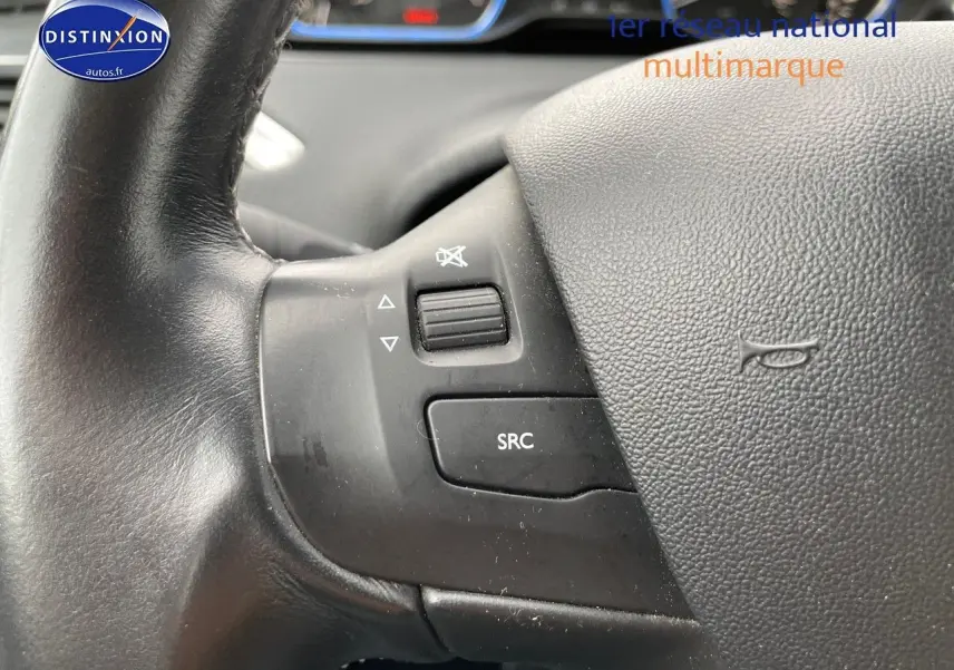 Gros plan sur les commandes audio au volant noir du Peugeot 2008 blanc nacré, version essence 2015.