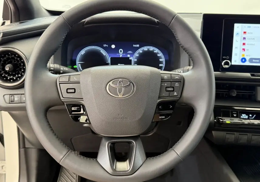 Vue intérieure centrée sur le volant cuir du Toyota C-HR 1.8 Hybride 140 Dynamic avec tableau de bord numérique.