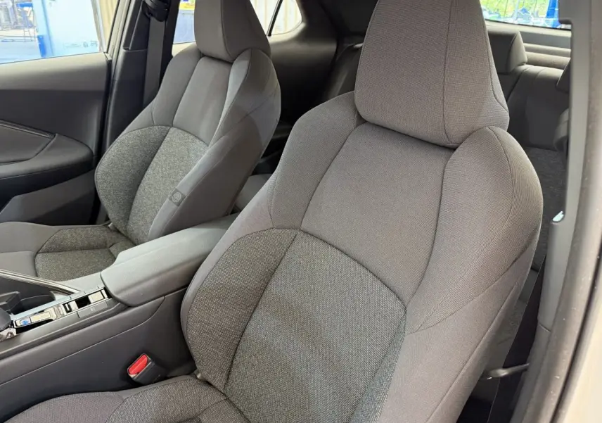 Vue intérieure rapprochée des sièges avant gris du Toyota C-HR 1.8 Hybride 140 Dynamic blanc, avec accoudoir central.