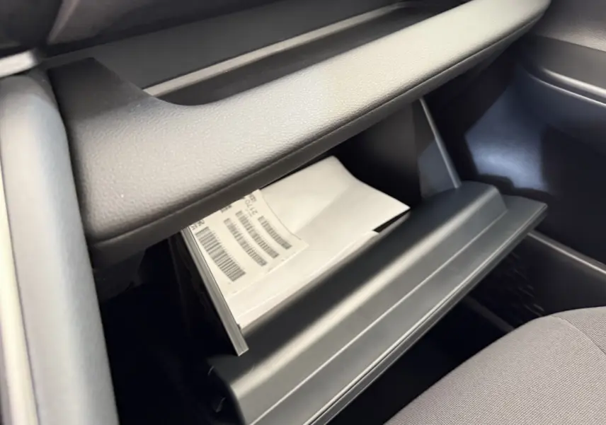 Intérieur du Toyota C-HR 1.8 Hybride 140 Dynamic 2024, vue sur la boîte à gants ouverte avec documents blancs visibles.