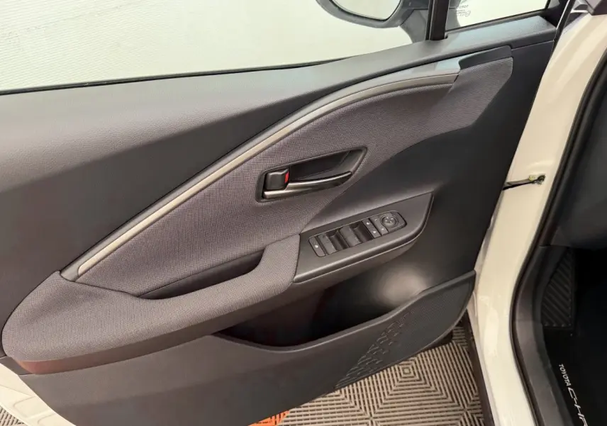 Vue intérieure côté gauche de la porte avant blanche du Toyota C-HR 1.8 Hybride avec commandes de vitres et poignée noire.