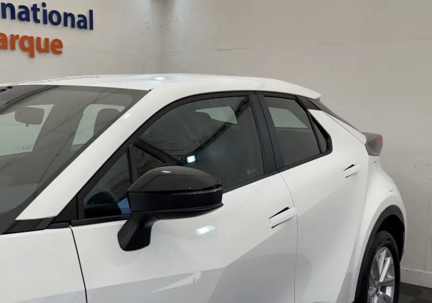 Vue de profil côté gauche d'un Toyota C-HR 1.8 Hybride blanc avec rétroviseur noir en intérieur showroom.