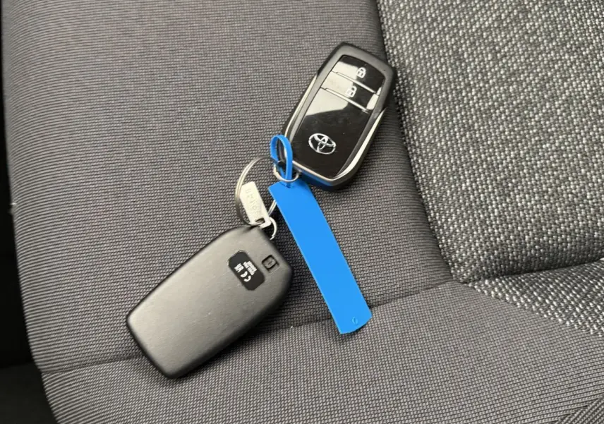 Gros plan sur la clé noire Toyota posée sur un siège tissu gris foncé, avec un porte-clés bleu visible.