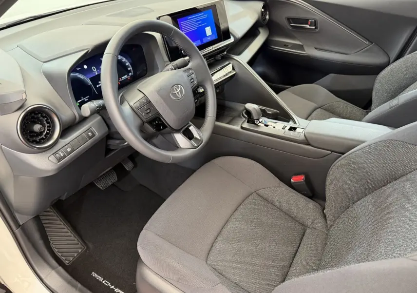 Intérieur avant droit du Toyota C-HR blanc 2024, volant cuir, écran tactile et sièges tissu gris.