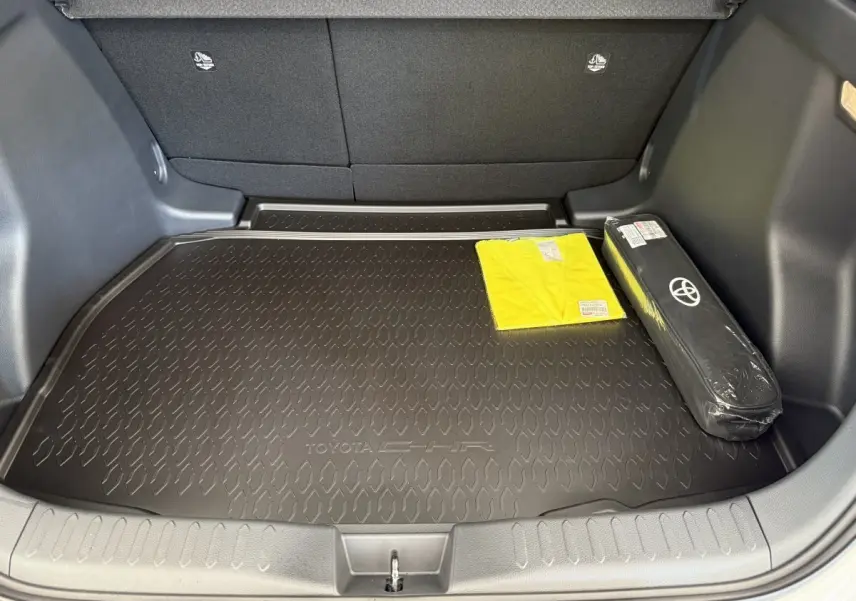 Coffre ouvert du Toyota C-HR blanc 2024 avec tapis de protection noir et accessoires de sécurité visibles.