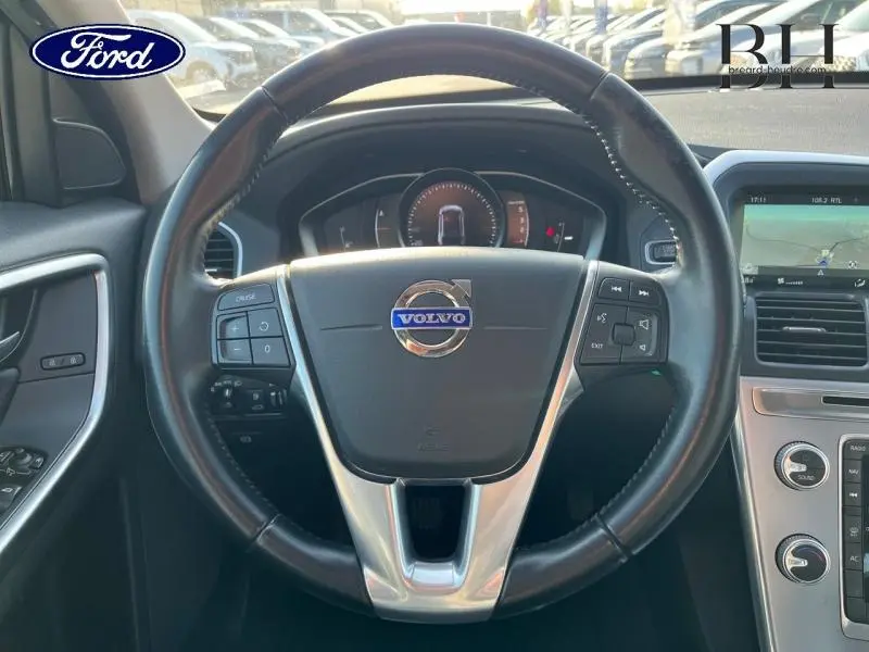 Vue intérieure centrée sur le volant cuir multifonction du Volvo XC60 gris Savile, avec tableau de bord et écran multifonction visible.