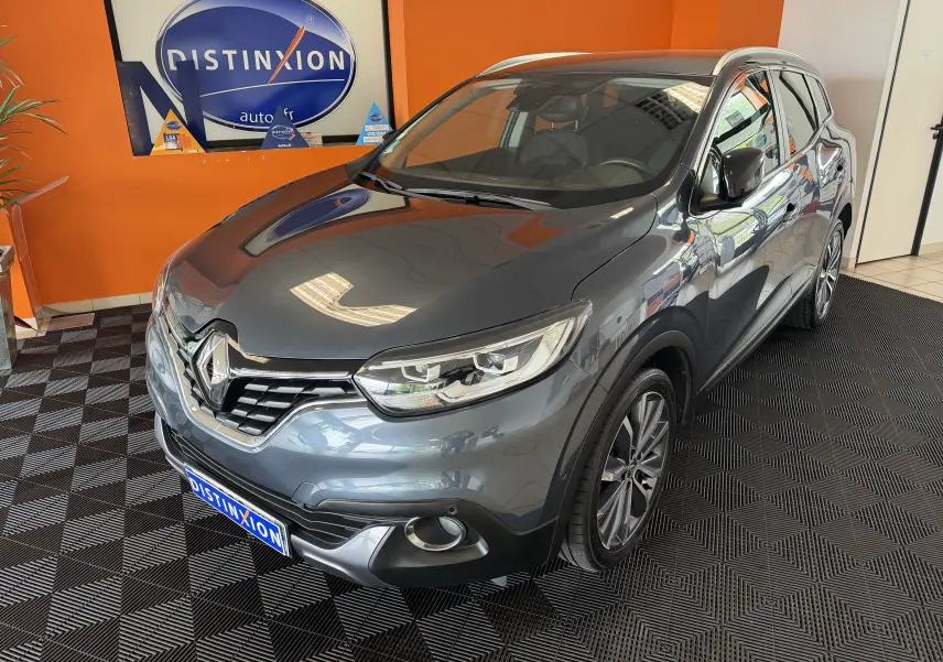 Renault Kadjar gris en 3/4 avant droit, avec jantes alliage et calandre distinctive dans un showroom.