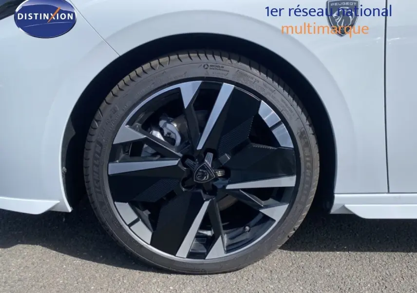 Gros plan sur la roue avant gauche de la Peugeot 308 blanche Okenite Metal avec jante alliage noire et argentée au design moderne.
