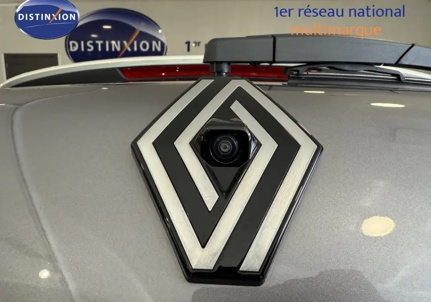 Gros plan sur la caméra arrière intégrée dans le logo Renault sur un capot gris cassiopée métallisé.