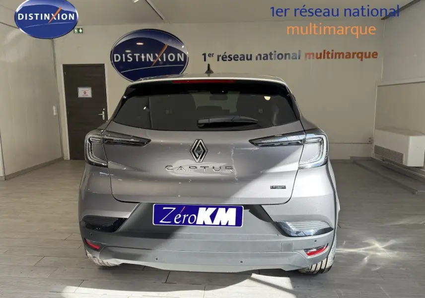 Vue arrière d'un Renault Captur gris Cassiopée métal avec toit gris, en intérieur showroom, badge hybride visible.