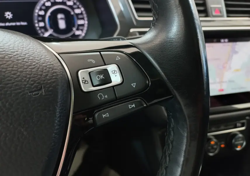Gros plan sur les commandes multifonctions côté gauche du volant cuir noir du Volkswagen Tiguan Allspace marron, avec tableau de bord numérique en arrière-plan.