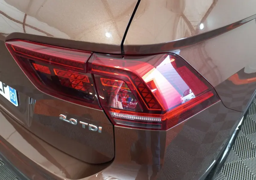 Gros plan sur le feu arrière droit marron métallisé du Volkswagen Tiguan Allspace 2.0 TDI 150 DSG7 avec logo visible.