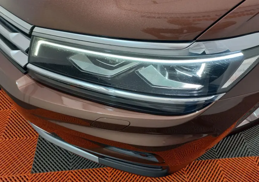 Gros plan sur le phare avant droit LED du Volkswagen Tiguan Allspace marron, avec calandre et pare-chocs visibles.