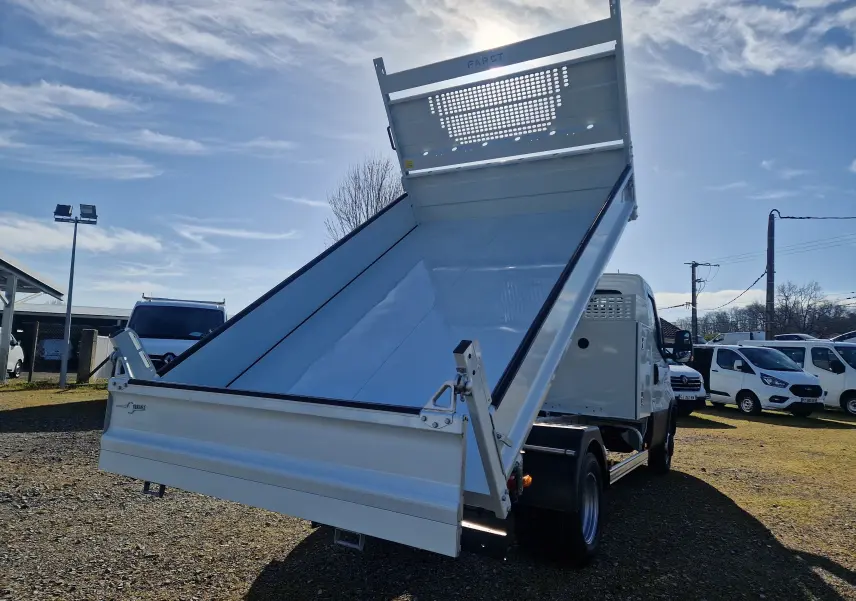 Vue arrière droite d’un Iveco Daily blanc avec benne relevée et coffre latéral, sur un terrain extérieur ensoleillé.