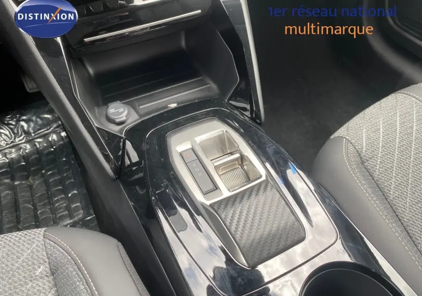 Gros plan sur la console centrale de la Peugeot 208 Hybrid 110ch, avec levier de boîte auto et sellerie tissu gris.