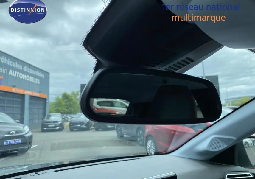 Vue intérieure centrée sur le rétroviseur intérieur d'une Peugeot 208 gris selenium, avec vue sur le parking extérieur.