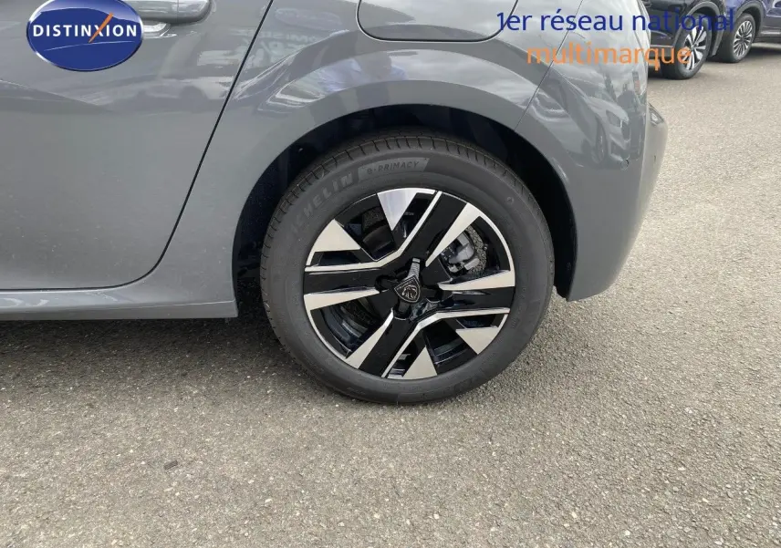 Vue rapprochée sur la roue arrière gauche d'une Peugeot 208 gris selenium métal, mettant en valeur la jante noire et argentée.