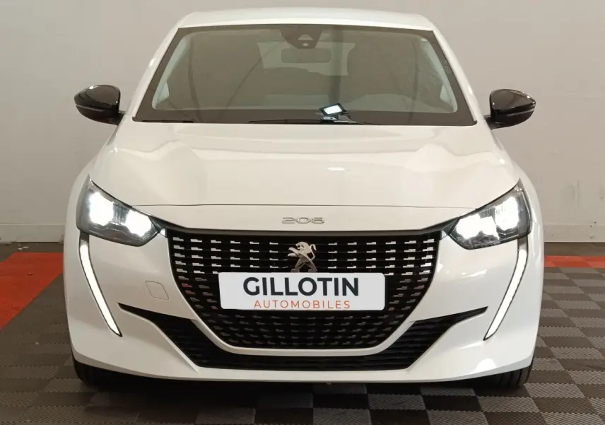 Vue avant d'une Peugeot 208 blanche 2023 avec phares LED allumés et calandre noire distinctive.